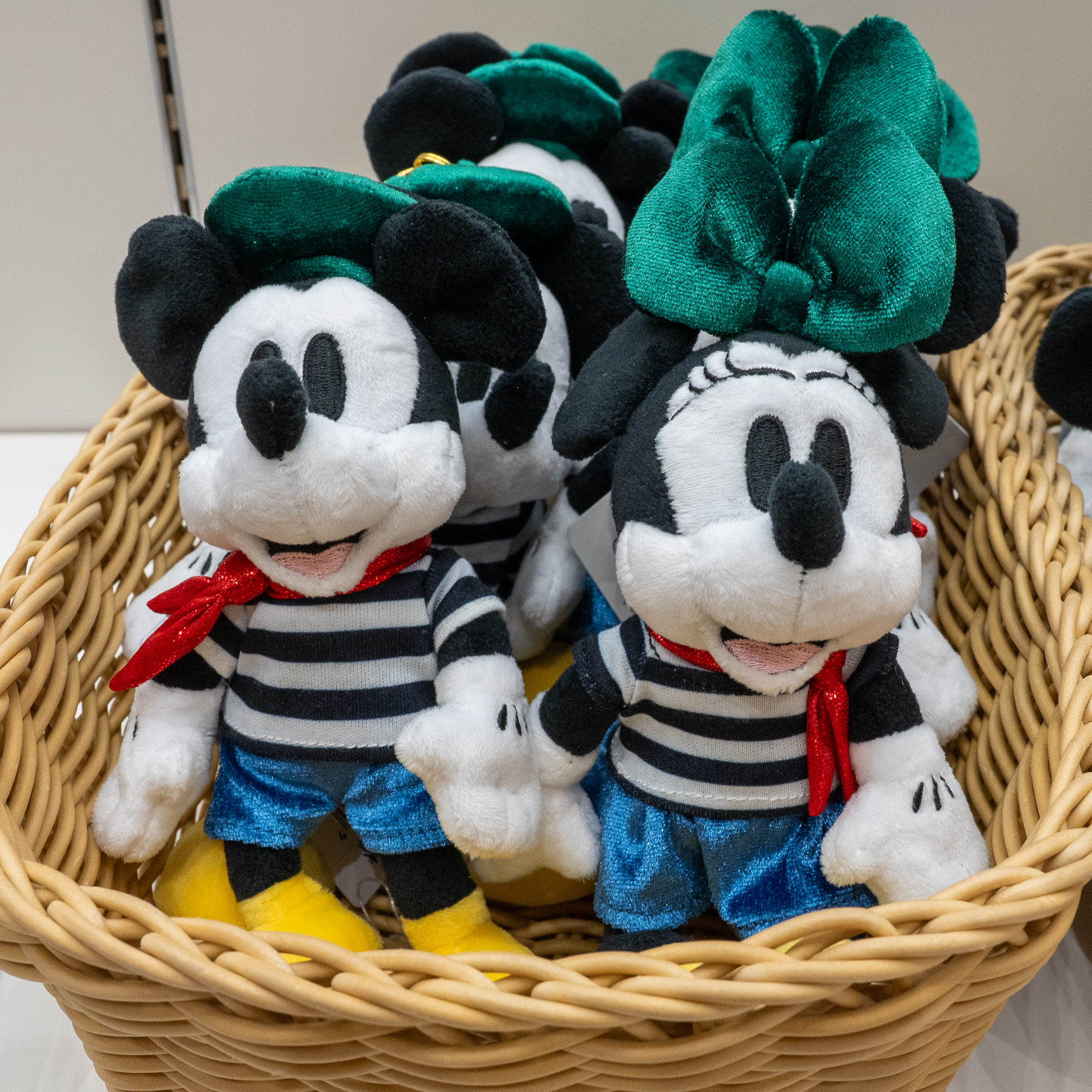 かごに入った、グリーンのベレー帽やリボンとボーダーの衣装のミッキーマウスとミニーマウスのぬいぐるみ