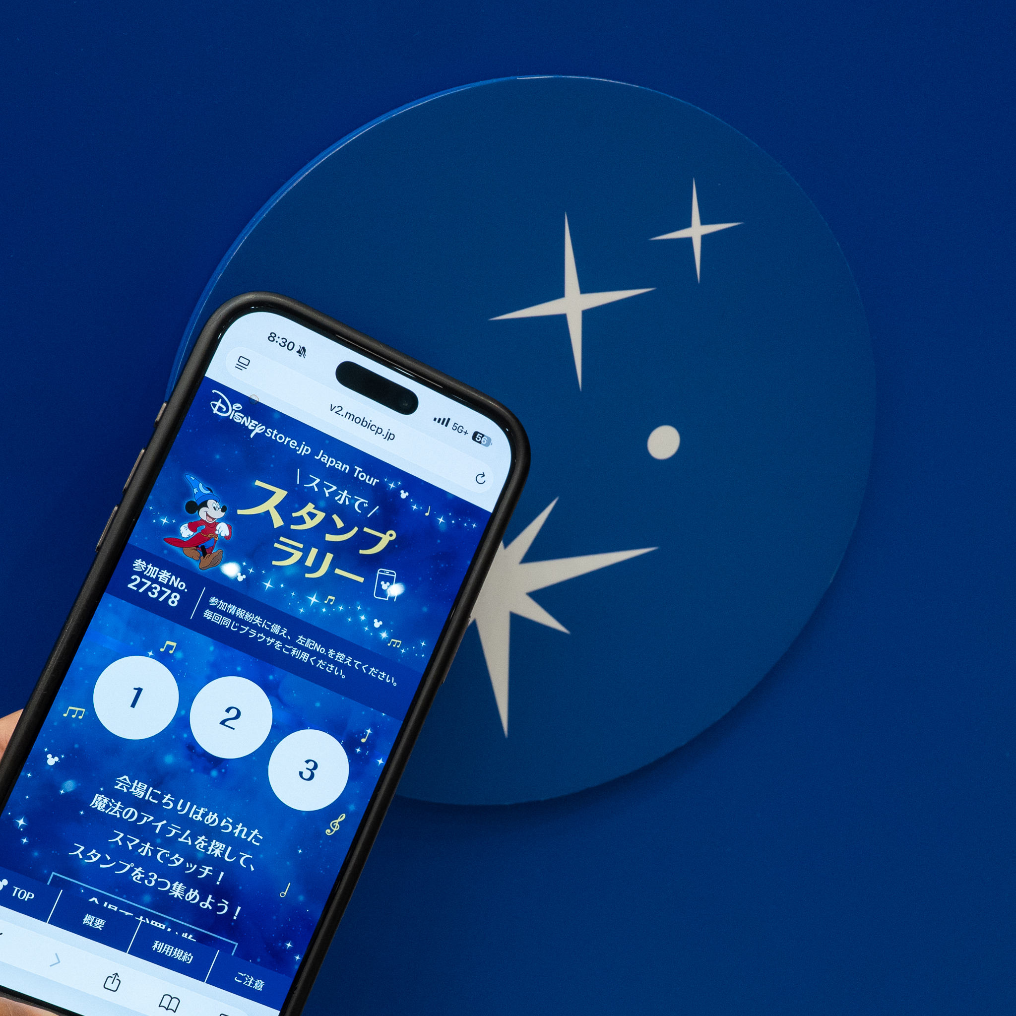 スタンプラリーの画面を表示したスマホと、星がデザインされたタッチポイント