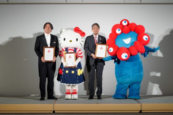 任命状を手にする志村健一氏とハローキティ、ミャクミャク