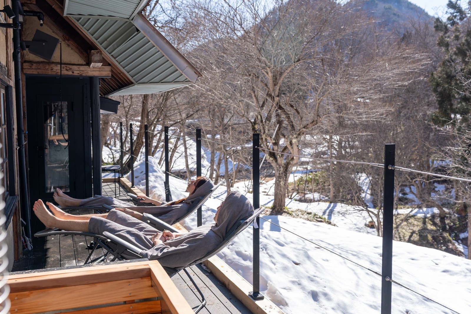雪景色の中のデッキでリクライニングチェアに横たわる2人