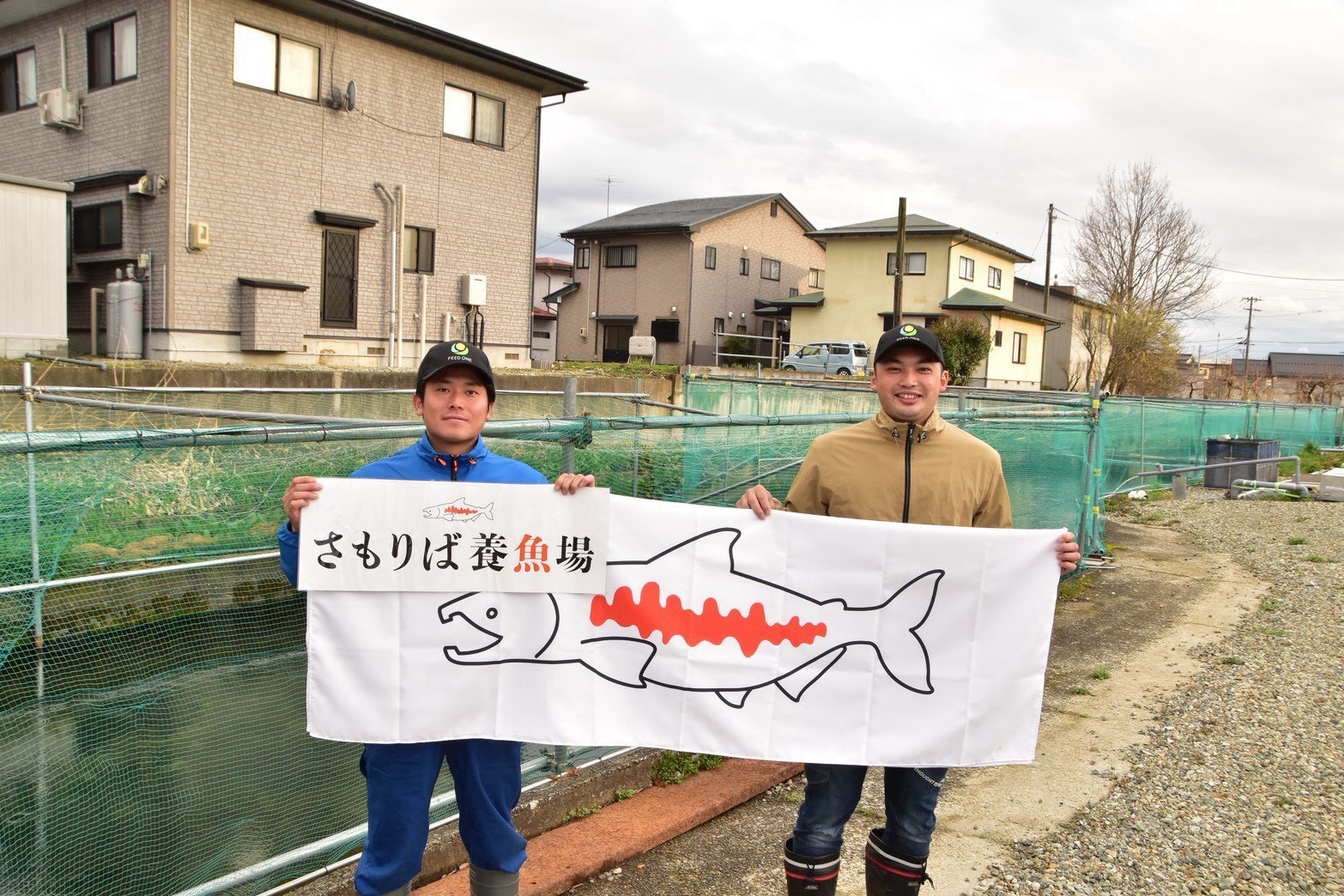 さもりば養魚場の看板を持つ2人